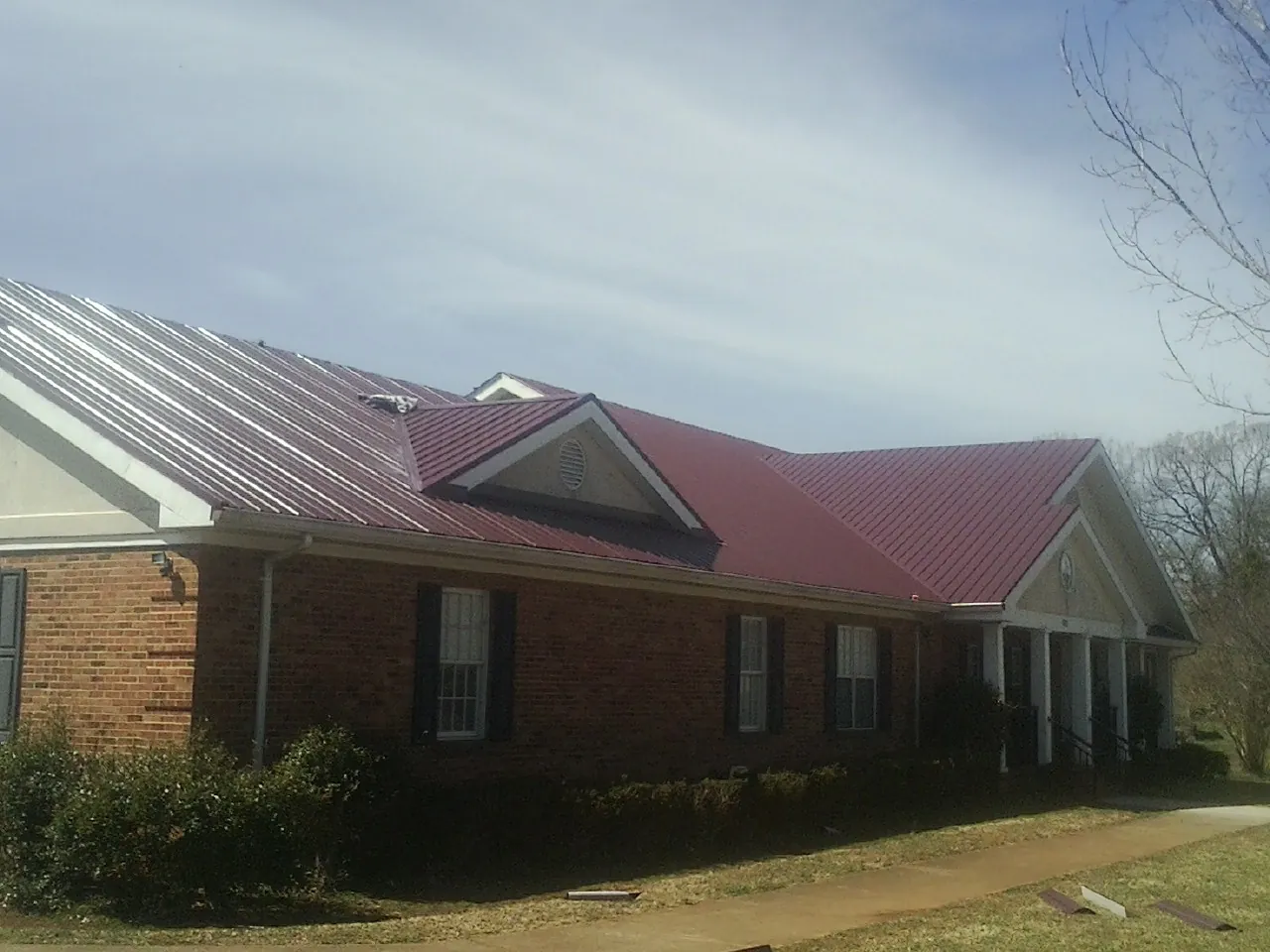 Red metal roof with gabled entries on a long brick building, from a Hail Damage Roof Repair job in Wakefield